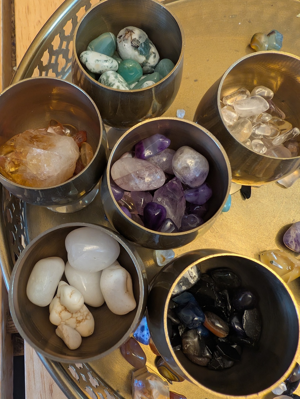 A closeup view of six bronze cups, each filled with a different colour of crystal (purple, black, white, orange, green and clear)